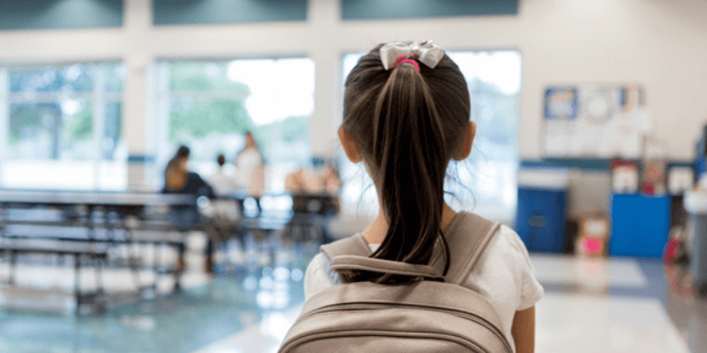 A young girl with a backpack alone at school