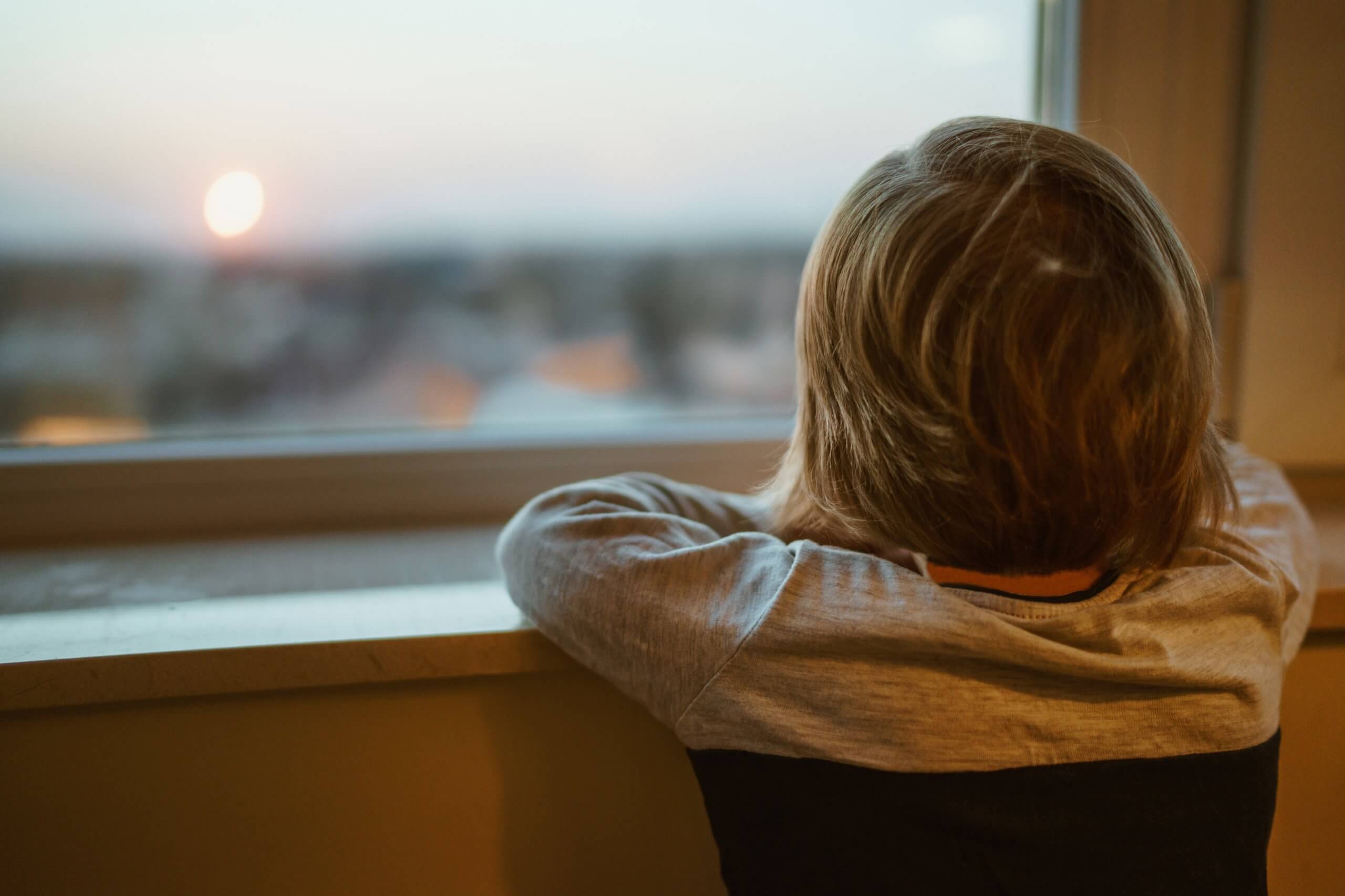 close up of back view young boy looking trough window