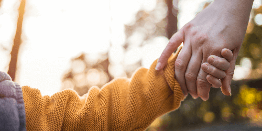 Child and adult holding hands outdoors