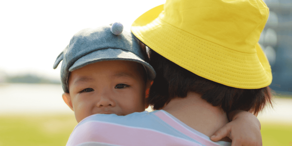 young child being held by mother. Both wearing hats and hugging.