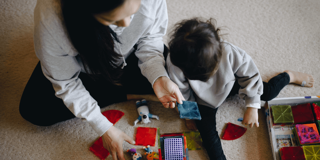 A woman and small child play with toys while sitting on the floor