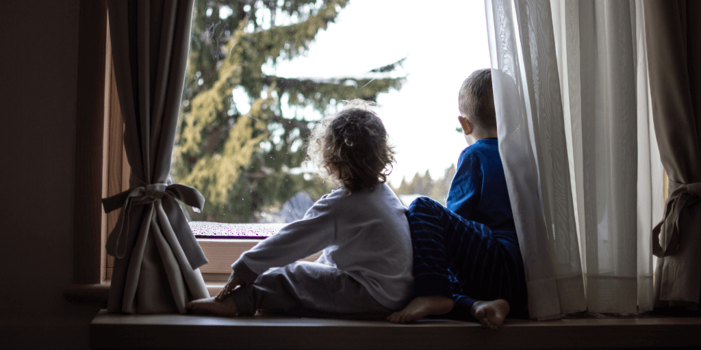 Two young children looking out window