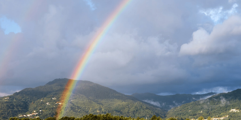 A rainbow with mountains and grey clouds in the background