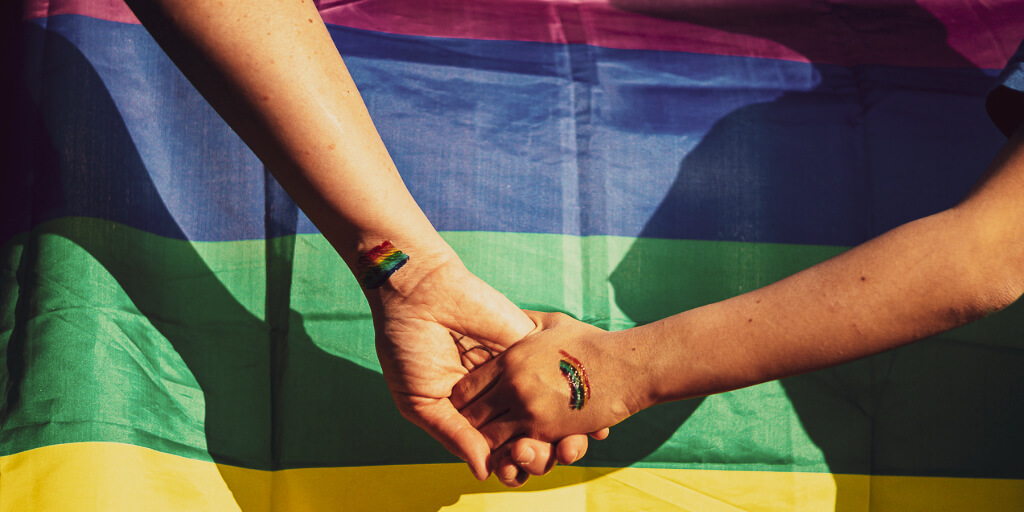 Parent and child holding hands in front of Pride flag