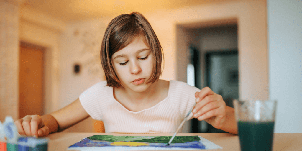 Introspective young girl painting at kitchen table