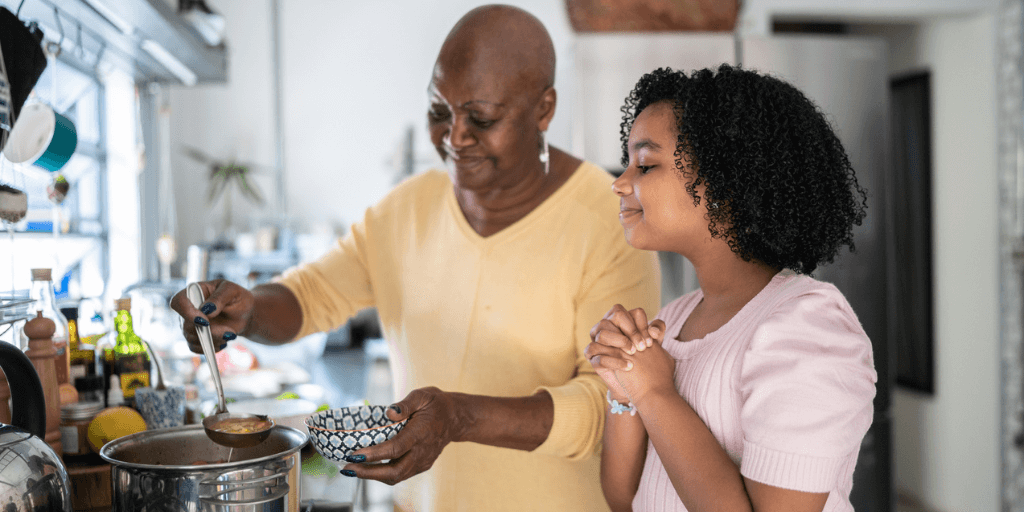 Grandmother serving soup bowl to granddaughter at home during family time.